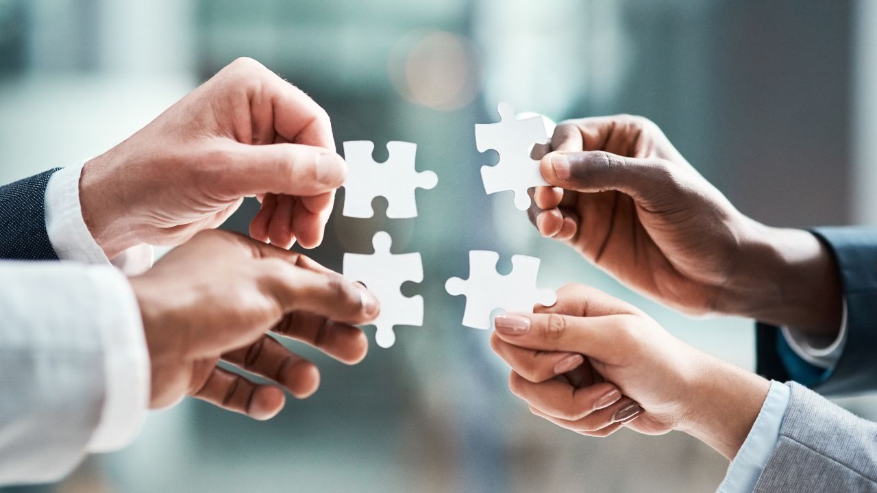 Four hands joining puzzle pieces together, symbolizing partnership and continuity