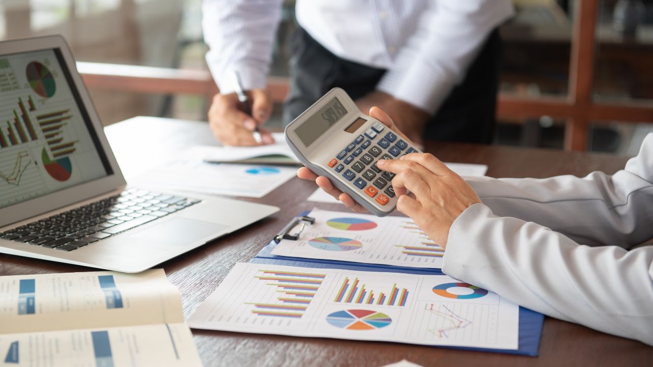 An accountant using a calculator while reviewing financial charts and reports